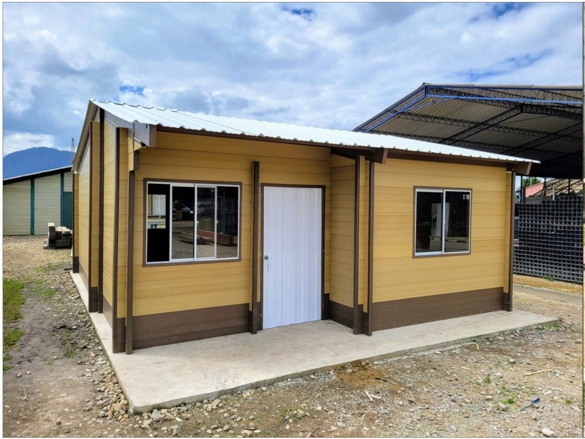 Casa prefabricada terminada, de fachada clara con zócalo café, dos ventanas y puerta blanca, sobre una placa de concreto.