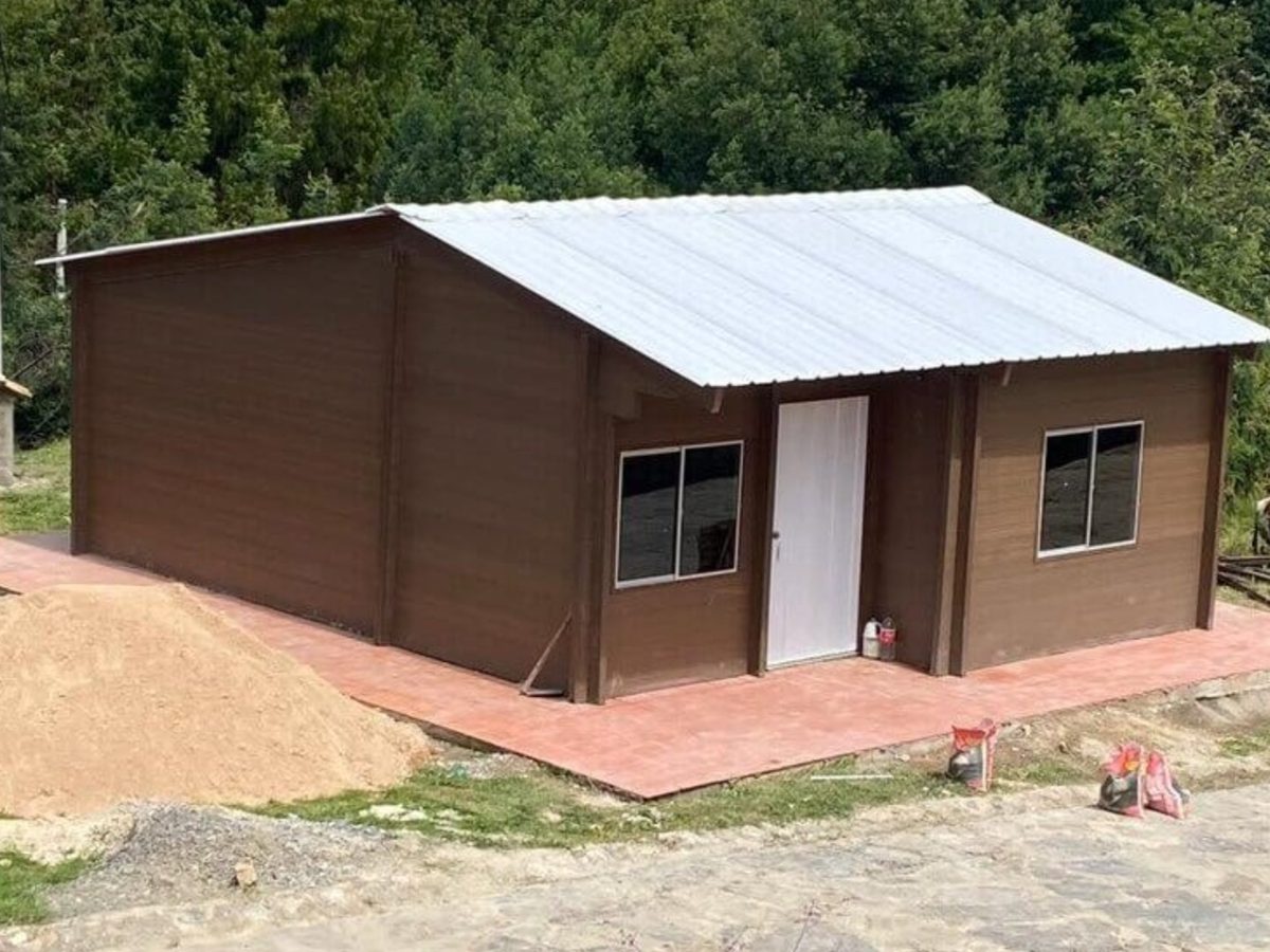 Casa prefabricada terminada, de fachada café con techo metálico a dos aguas, instalada en ladera.